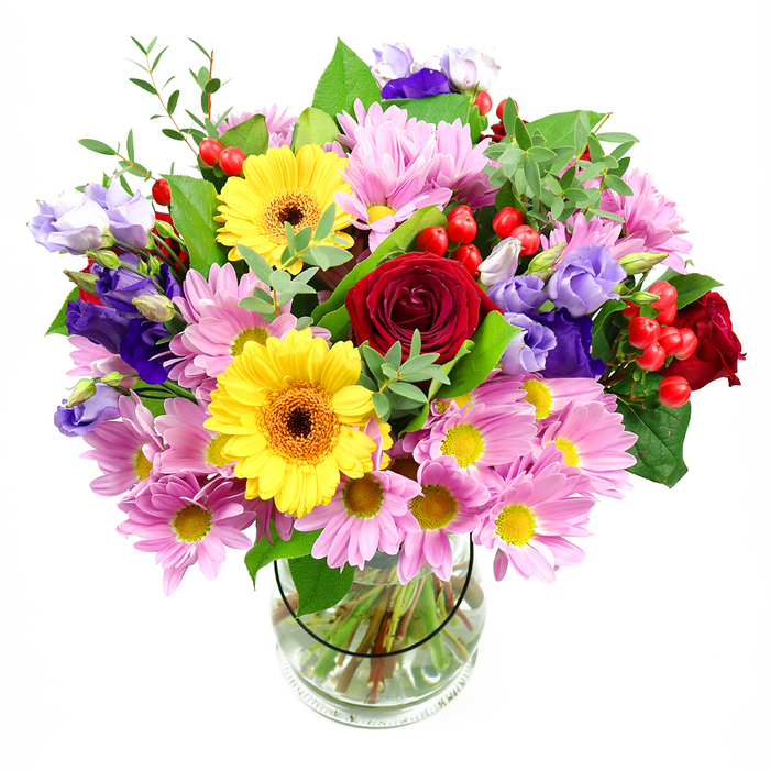 Set against a crisp white background, a tall, mixed-colour bouquet in a clear glass vase captures the eye with its harmonious blend of richness and cheer. At the heart of the arrangement, deep red roses open in velvety spirals, conveying a sense of romance and giving the piece a strong, confident core. Nestled close by, bright yellow gerbera daisies with warm brown-orange centres glow like miniature suns, immediately brightening the palette and drawing the gaze. Surrounding these central flowers, an abundance of soft pink and lilac daisies or chrysanthemums spills outward, their many slender petals and tiny yellow eyes creating a cloud of gentle colour that feels light and welcoming. Threaded delicately among them, elegant stems of purple and lavender lisianthus rise and curve, their bell-shaped blooms and ruffled edges adding cool sophistication and a little movement, as if caught by a soft breeze. Scattered throughout, shiny red hypericum berries punctuate the arrangement in rounded clusters, bringing a fresh, modern texture that contrasts nicely with the softer petals. The bouquet is supported by an artful mix of greenery in varied tones-from deep, broad leaves that ground the piece to finer, lighter sprigs that echo new spring growth, similar to the layered foliage you'd notice wandering down Sheen Lane or entering the green expanses around East Sheen. Through the glass vase, straight, neatly cut stems can be seen clearly in the fresh water, highlighting the thoughtful construction by an experienced florist at Florist East Sheen. The overall mood is joyful yet composed, making this mixed bouquet perfectly suited to marking birthdays, anniversaries, or house-warmings in the local area, or to simply bring a sense of celebration into an everyday East Sheen home.